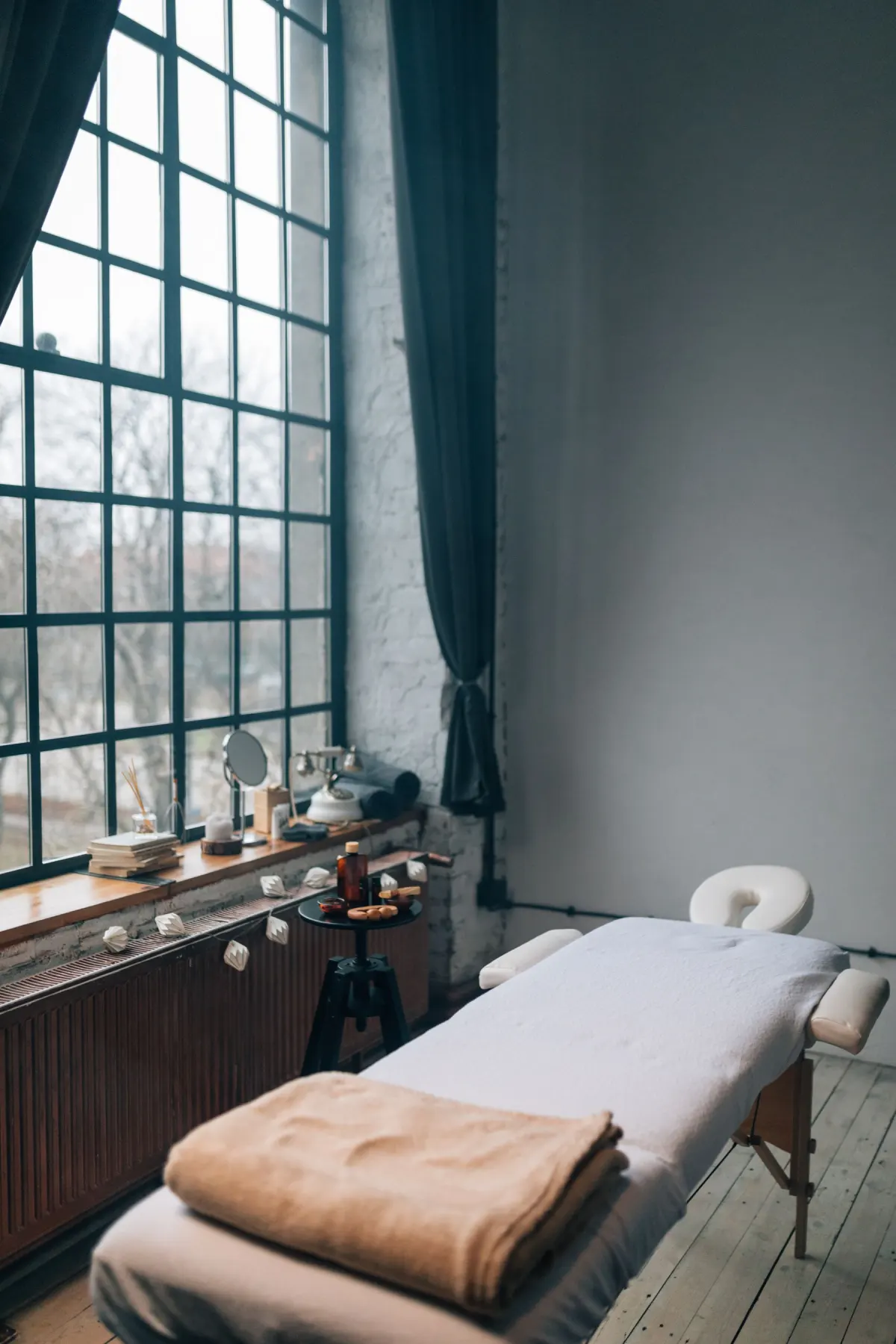 A quiet treatment room with a tall window and a treatment table
